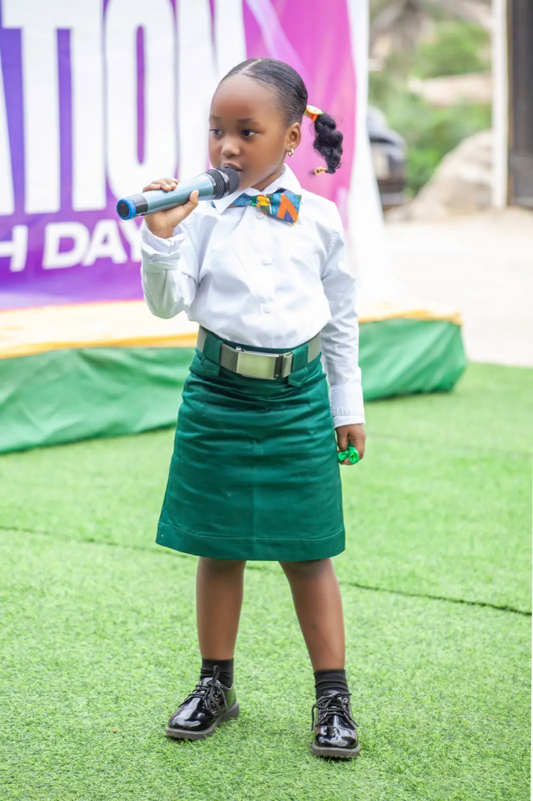 A young pupil in the green and white school uniform speaking into a microphone at a school event