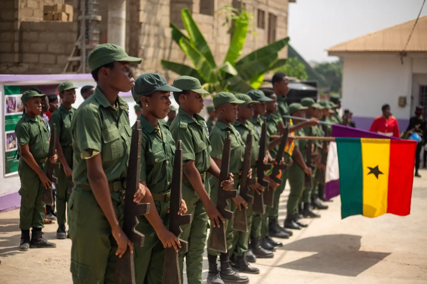 Pupils in green parade uniform standing at attention beside the flag of Ghana